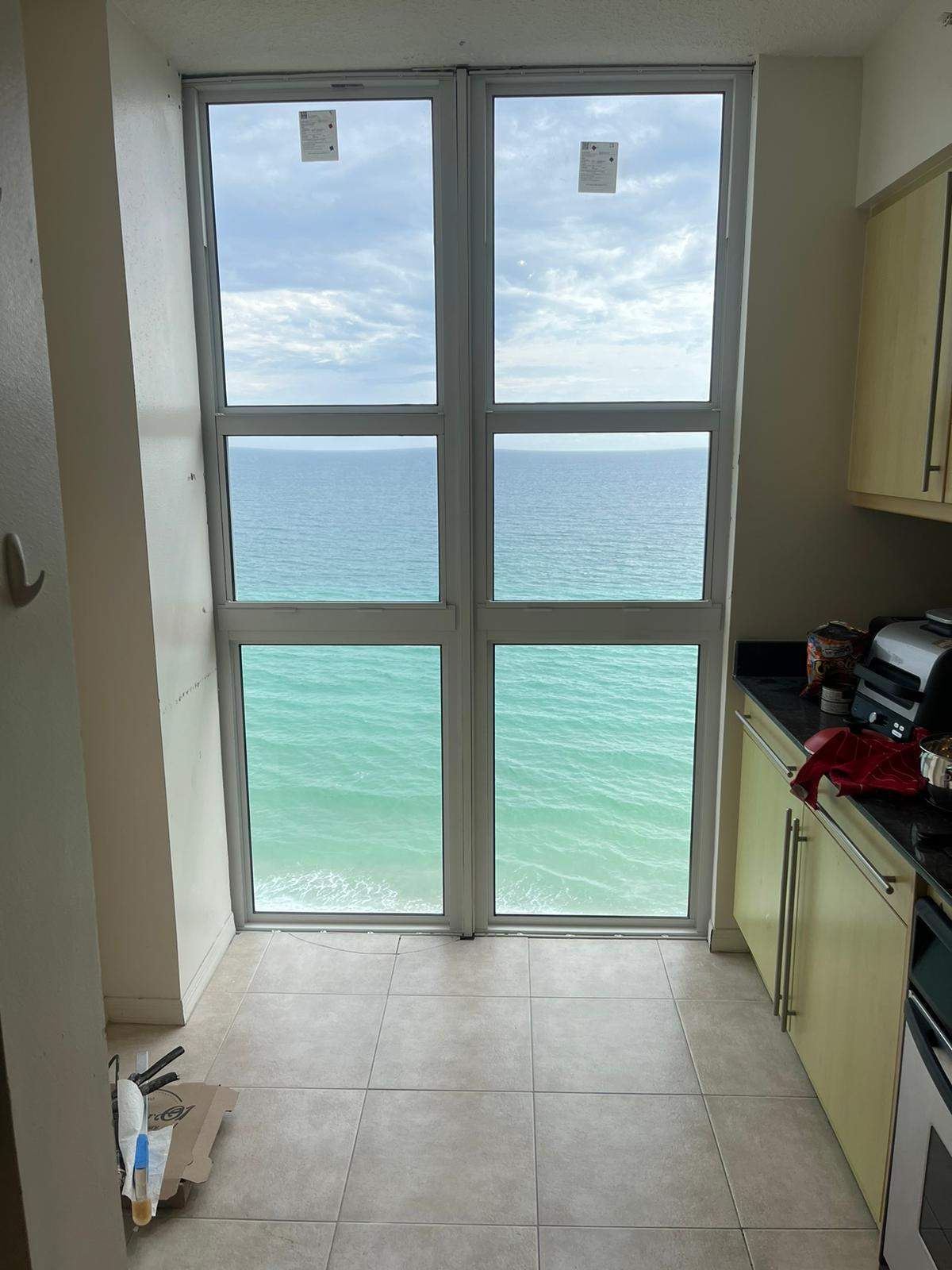Newly installed floor-to-ceiling 6-lite mulled aluminum impact window wall inside an oceanfront high-rise condominium overlooking the turquoise Atlantic Ocean