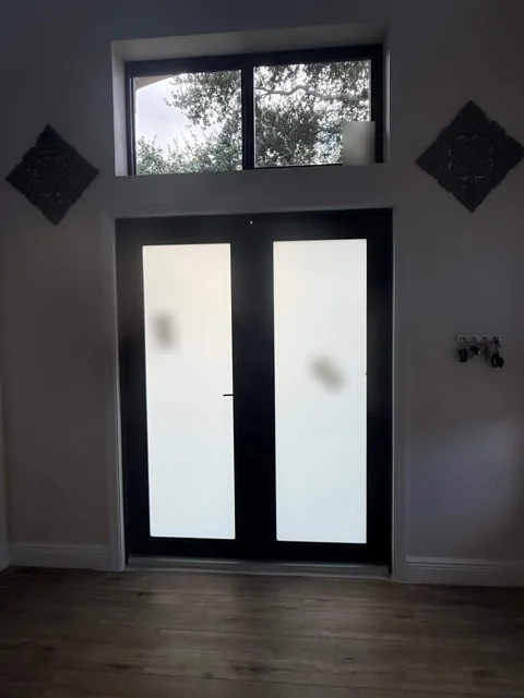 Inside view of a black-frame double French impact door with frosted glass and a transom window above it