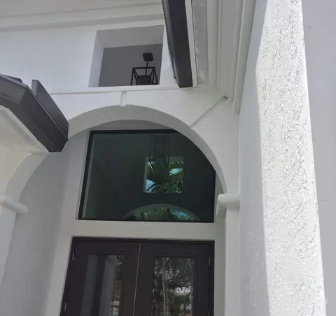 Bronze full-glass double impact entry door with a large picture window set in the arched opening above it