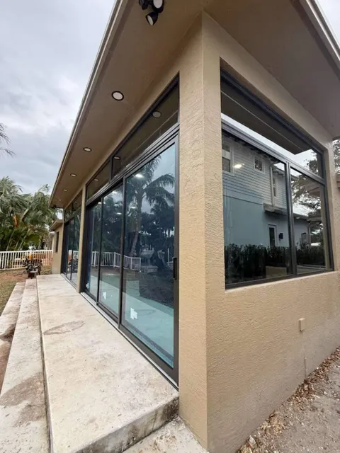 Bronze-frame impact sliding glass doors and corner windows on a tan stucco addition