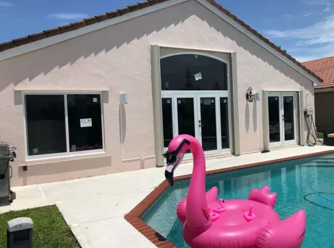 Pink stucco home by a pool with new white impact windows and French doors under a tall arched window