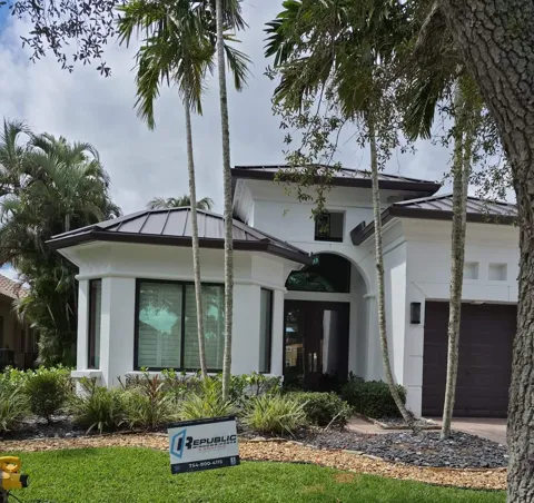 White stucco home with bronze-frame impact windows, a dark double entry door under an arched window, and a Republic yard sign on the lawn
