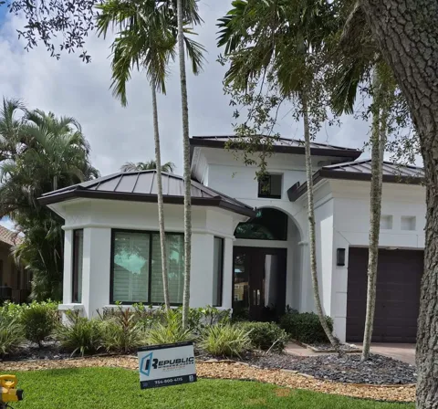 White two-story home with dark-frame impact windows and a dark glass entry door under an arched window, with a Republic yard sign on the lawn
