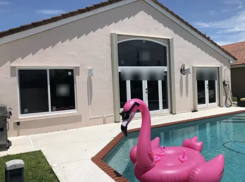 Back of a pink stucco home by a pool with white impact windows, French doors under an arched transom, and a second French door