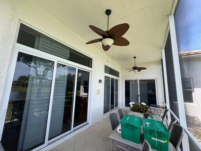 White-frame impact sliding glass doors and fixed transom windows along a covered patio lanai with ceiling fans