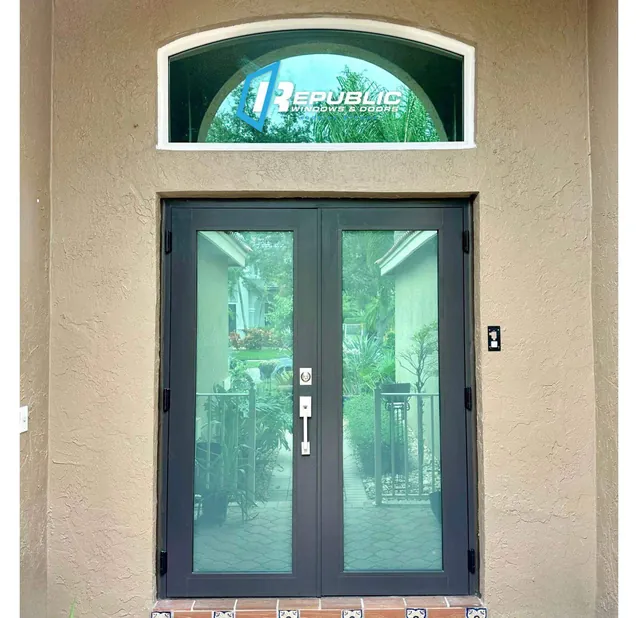 Dark bronze double French impact doors with a white-frame arched eyebrow transom window above