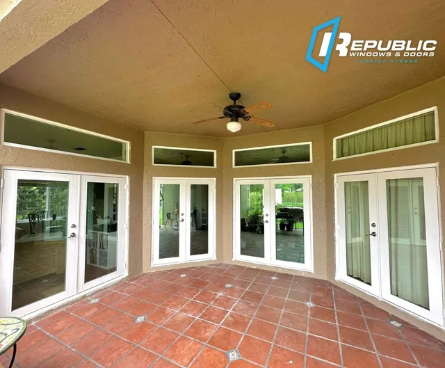 Multiple pairs of white-frame impact French doors with rectangular fixed transom windows around a Saltillo-tiled patio
