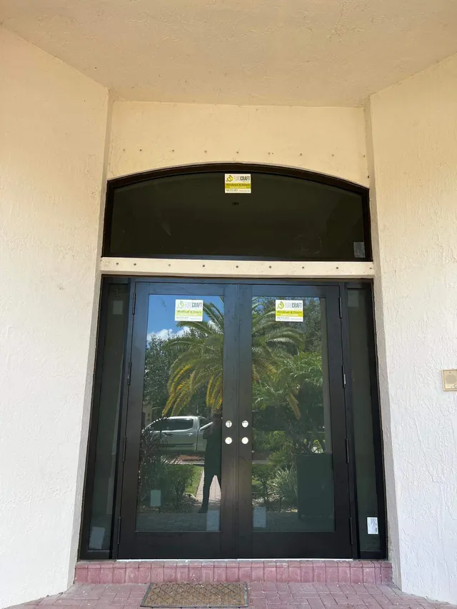 Dark bronze double impact entry doors flanked by full-height glass sidelights under an arched eyebrow transom window