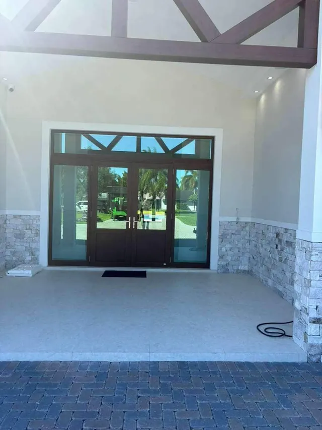Dark bronze double impact entry doors with glass sidelights and a gridded rectangular transom window under a covered porch