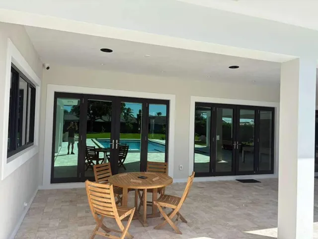 Two sets of dark-frame double impact French doors flanked by matching fixed glass sidelights on a covered travertine patio
