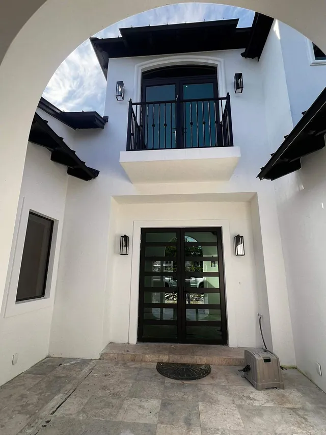 Dark-frame double impact French doors with horizontal glass lites on the ground floor and second-story balcony of a modern home