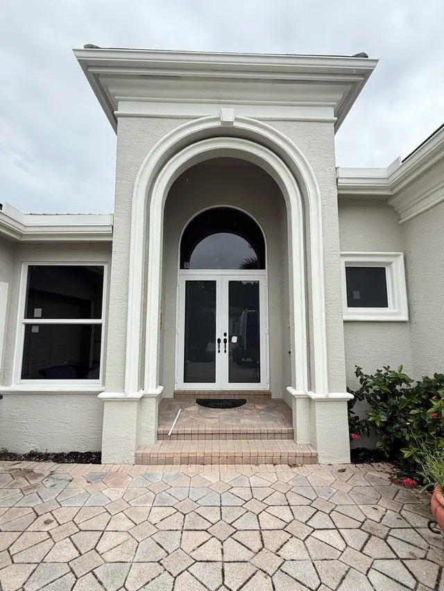 White-frame arched double impact French doors with an arched transom window inside a grand stucco portico