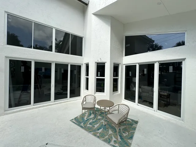 Two sets of white-frame three-panel impact sliding glass doors with large fixed and trapezoidal transom windows on a modern patio