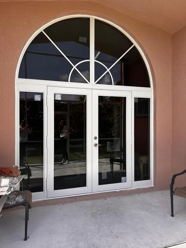 White-frame double impact entry doors with glass sidelights and a decorative arched sunburst transom window