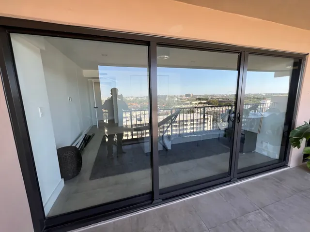Dark-frame three-panel impact sliding glass door with Low-E solar control glass on an upper-floor balcony