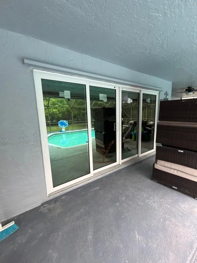 Four-panel white-frame impact sliding glass door opening from a covered porch to a backyard swimming pool
