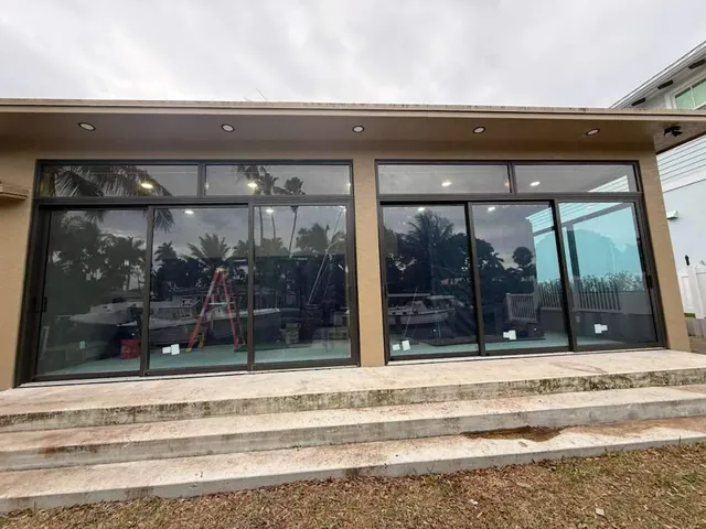 Wide dark-frame impact sliding glass doors with matching fixed transom windows across the rear elevation of a home