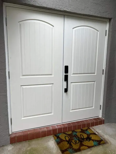 White double impact fiberglass doors with arched plank panels and black hardware