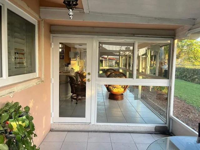 White-frame Florida room enclosure with a full-lite impact glass door, fixed picture lower pane, and horizontal roller upper window on a tiled patio
