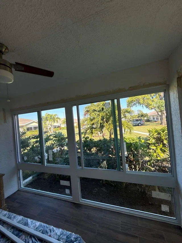 Interior view of a Florida room enclosure with wood-look flooring, two fixed lower impact glass panes, and two horizontal roller windows above