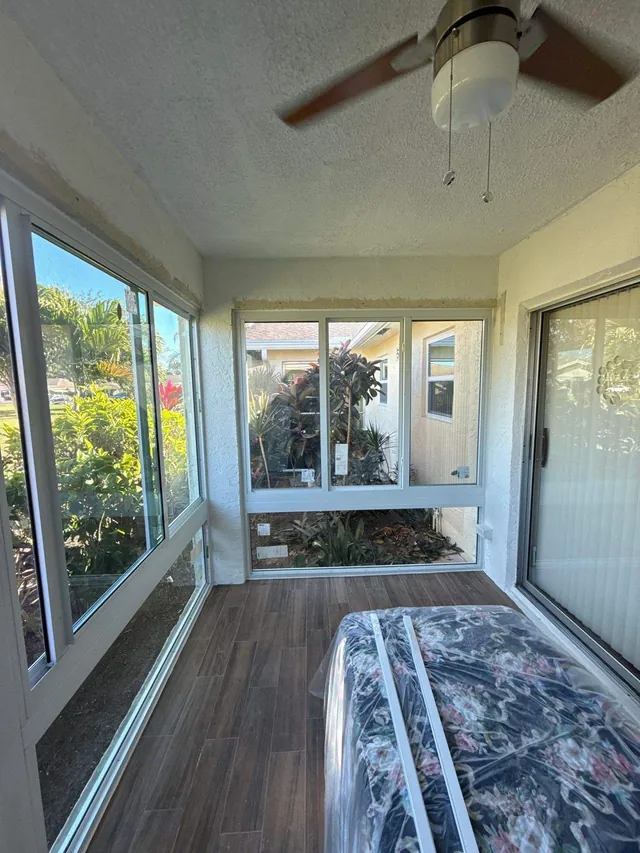 Interior view of an enclosed Florida room with horizontal roller impact windows along the side wall and a sliding glass door entry