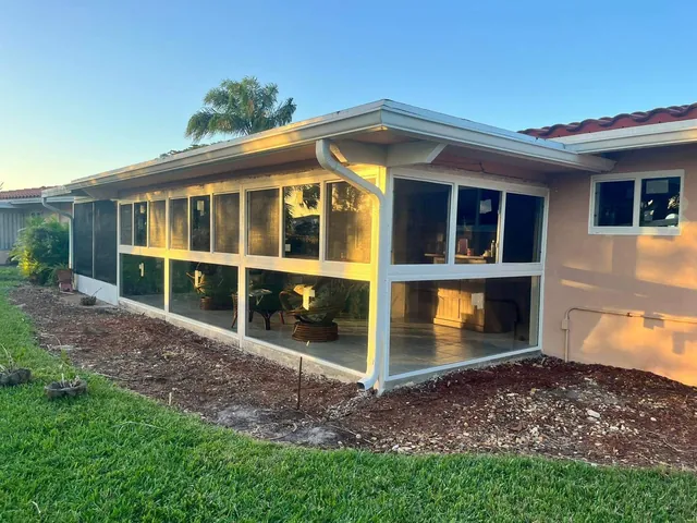 Full exterior span of a single-story white-frame Florida room enclosure with fixed picture glass and horizontal roller windows under a shingle roof