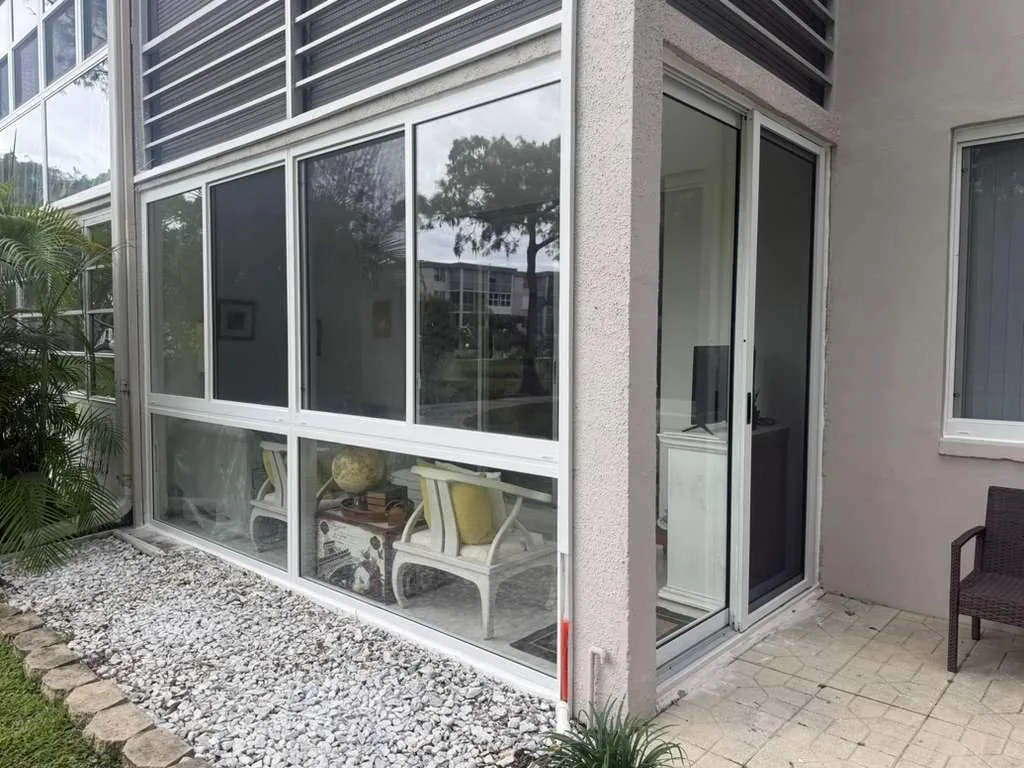 Ground-floor Florida room enclosure with three-bay fixed and horizontal roller impact windows and a white-frame glass entry door