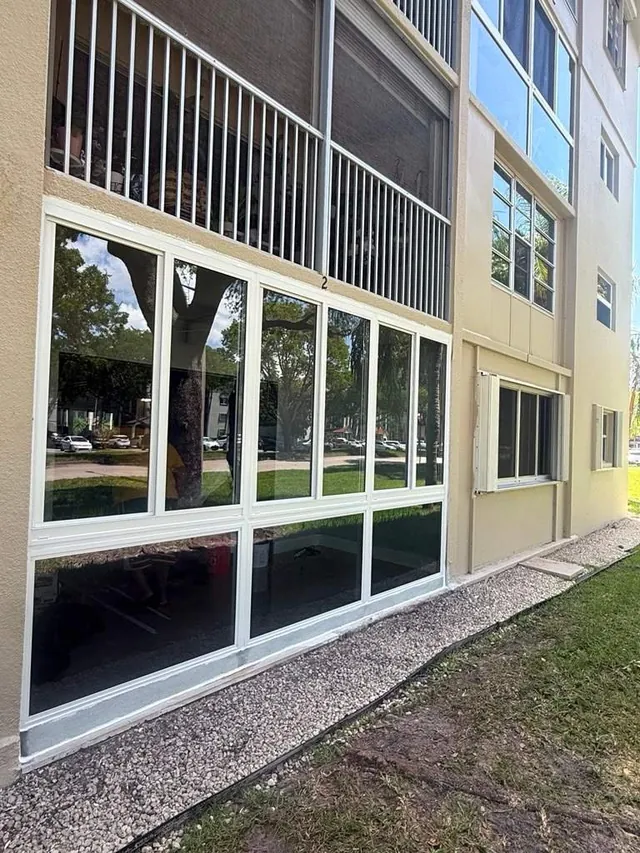 Exterior vertical view of a white-frame Florida room enclosure with fixed bottom glass panels and horizontal roller windows above