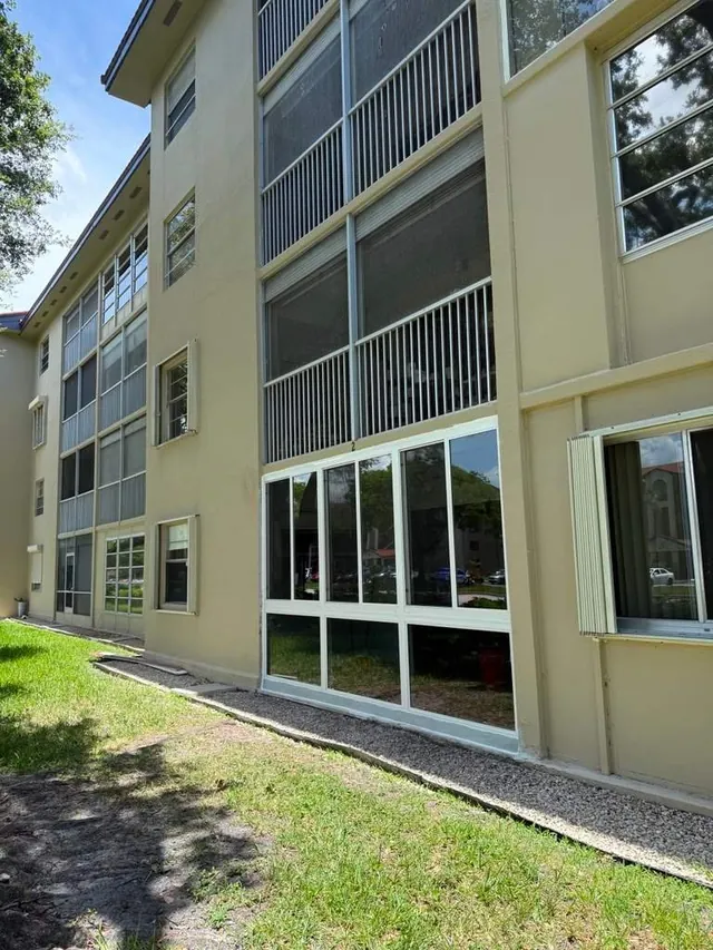 Exterior view of a ground-floor condo patio enclosed with white-frame fixed impact glass below and horizontal roller windows above