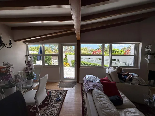 Finished interior of a Florida room enclosure with wood-beam ceiling, single-hung impact windows, and a full-lite single glass door opening to the yard