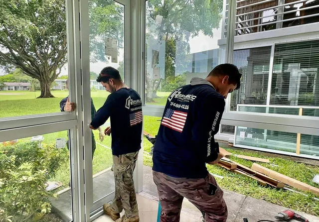 Two Republic Windows & Doors installers fitting a white-frame impact glass assembly into a Florida room enclosure opening