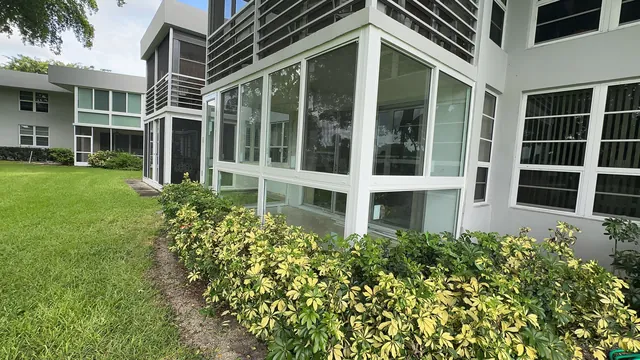 Wide exterior view of a multi-story building with a ground-floor white-frame impact glass Florida room enclosure
