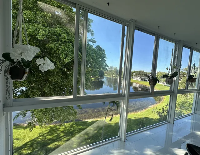 Interior corner view of a waterfront Florida room enclosure with white-frame fixed lower glass and horizontal roller upper windows overlooking a lake