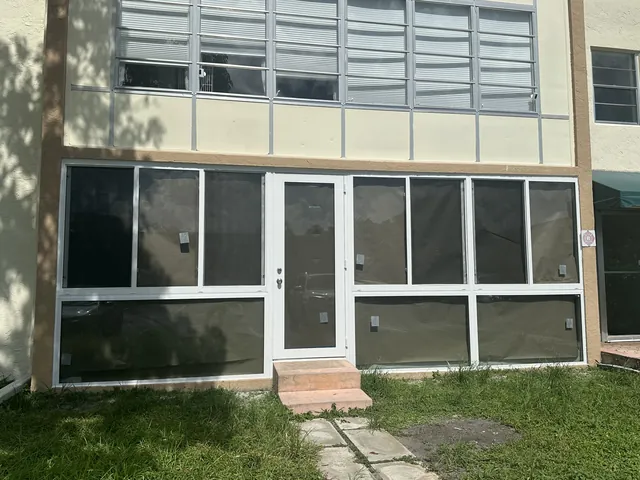 Symmetrical ground-floor Florida room enclosure with a centered white-frame single impact glass door flanked by fixed and horizontal roller windows
