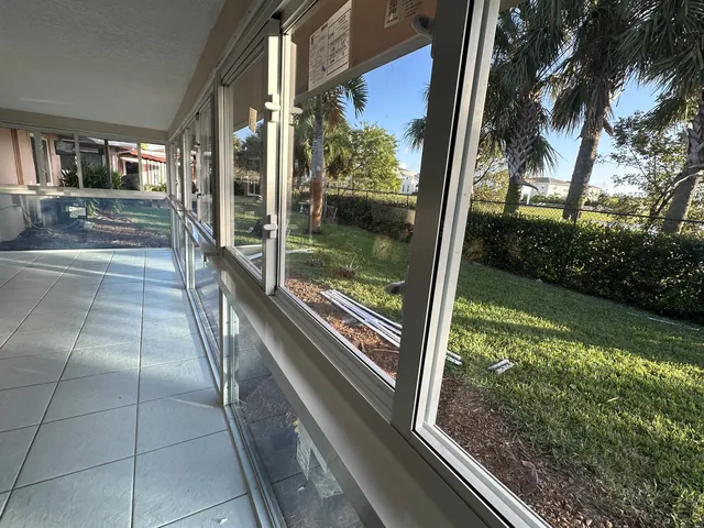Interior view of a newly installed white-frame Florida room window wall with horizontal mullions and Low-E impact glass facing a landscaped lawn