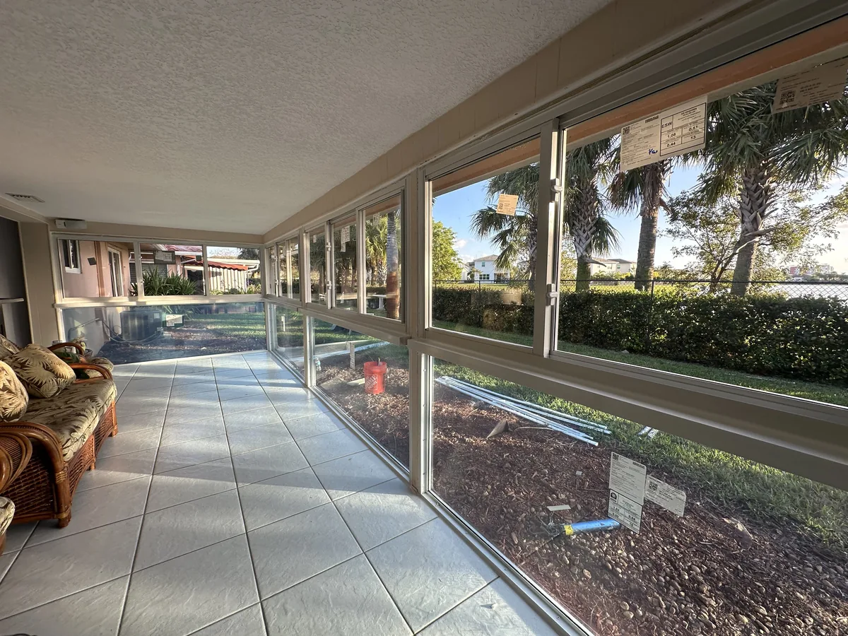 Wide interior view of a tiled Florida room enclosure with continuous white-frame fixed and horizontal roller impact windows
