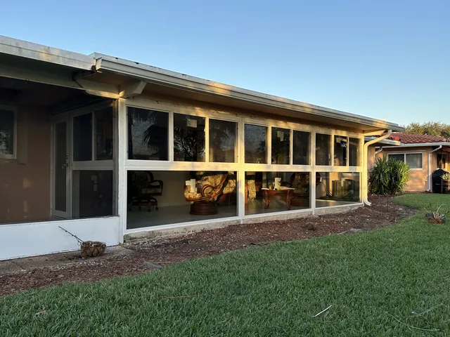 Exterior side view of a wrap-around white-frame Florida room enclosure attached to a single-story South Florida home
