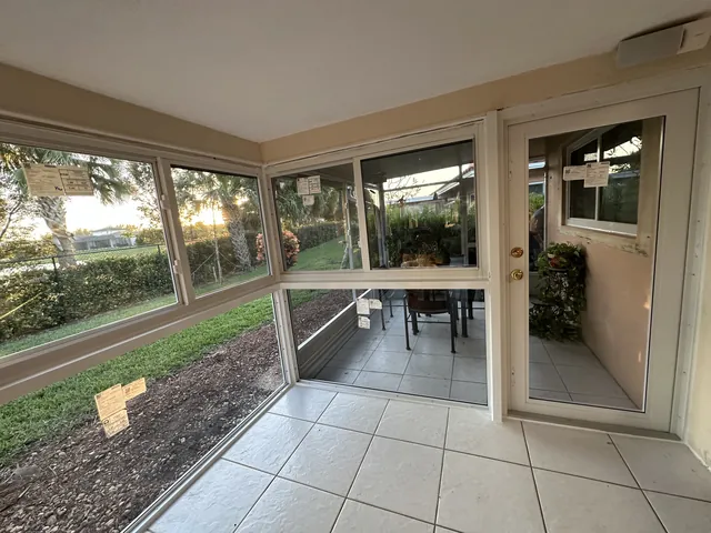 Interior view of a tiled Florida room enclosure showing a white-frame single impact glass door and full-height window wall
