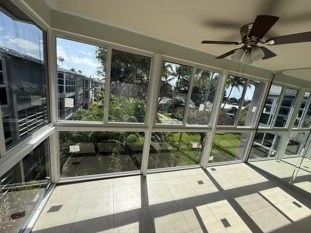 Corner interior view of an upper-floor Florida room enclosure with white-frame impact windows overlooking tropical palms