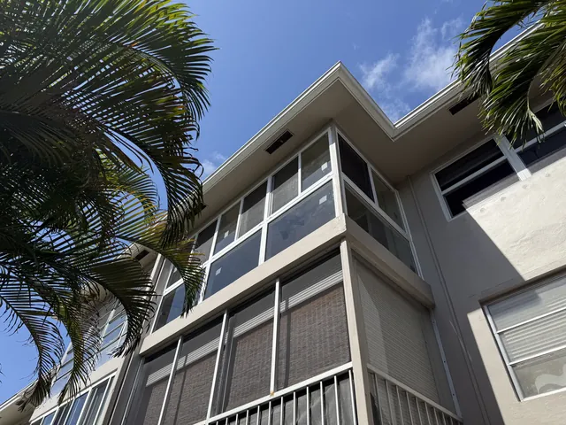 Exterior view looking up at a second-story white-frame impact glass Florida room enclosure above a ground-floor lanai