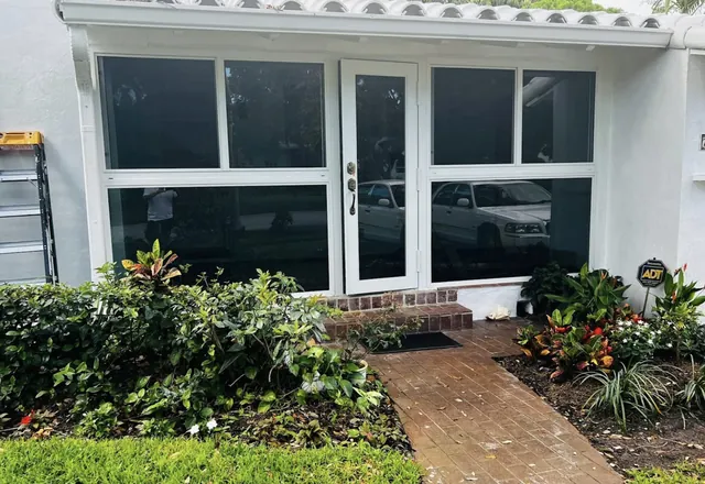 Front exterior view of a white-frame Florida room enclosure with a single impact glass entry door, fixed picture lower panes, and Low-E tinted glass