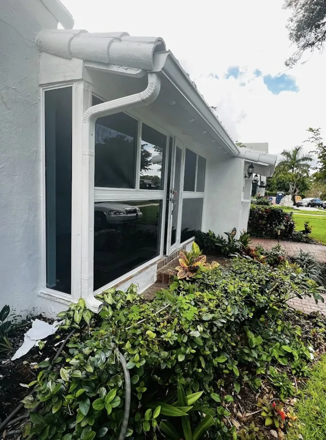Exterior corner view of a white-frame Florida room enclosure with double glass doors, sidelights, transom windows, and a bay window return
