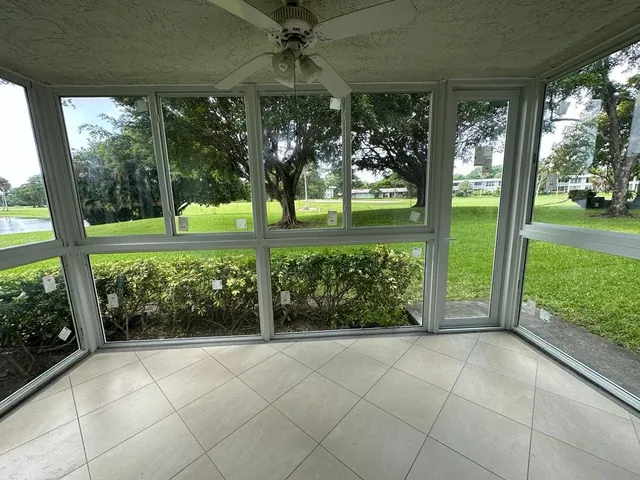 Panoramic interior view of a wide Florida room enclosure with white tile floors, ceiling fan, and continuous white-frame impact windows