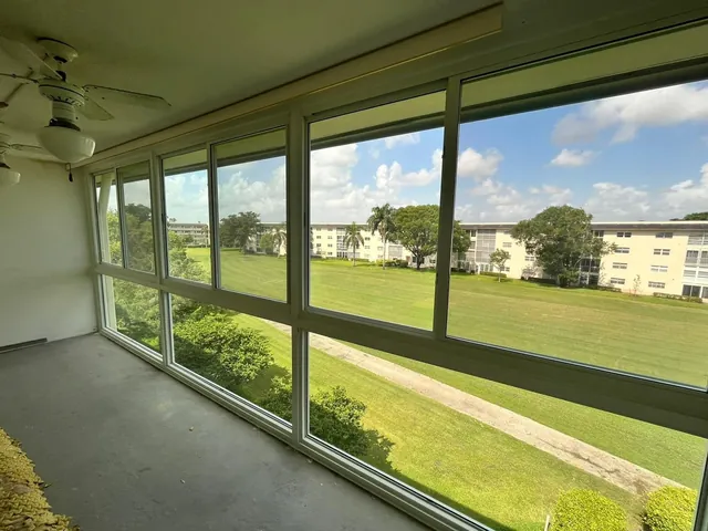 Interior view of an enclosed balcony Florida room with white-frame horizontal roller impact windows overlooking a golf course