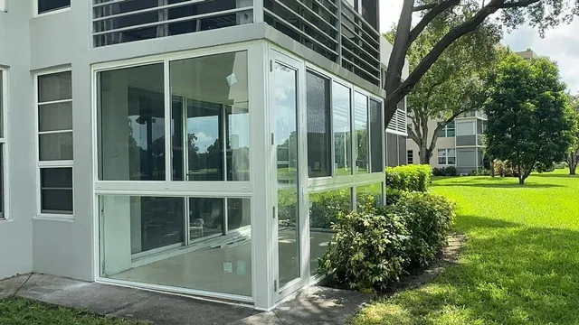 Daytime exterior view of a ground-floor white-frame Florida room enclosure with large Low-E impact glass panels