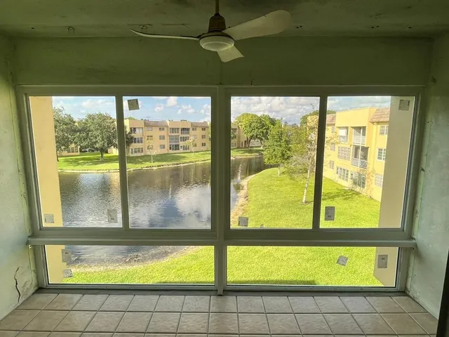 Upper-floor Florida room interior with white-frame horizontal roller and fixed impact windows overlooking a community lake
