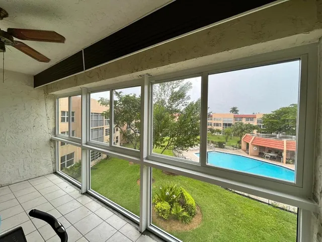 Interior view of an upper-floor Florida room enclosure with white-frame impact windows overlooking a community swimming pool