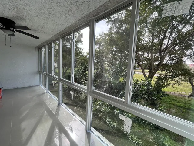 Sunlit interior of a tiled Florida room enclosure with white-frame fixed lower panes and horizontal roller windows facing a wooded preserve