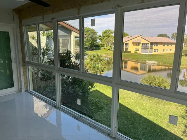 Wide interior view of a lakefront Florida room with glossy tile flooring, white-frame fixed lower windows, and horizontal rollers above