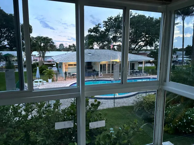 Interior corner close-up of white-frame horizontal roller impact windows in a Florida room overlooking a community pool deck